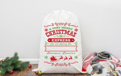 White Christmas sack with festive text and graphics on a wooden surface with Christmas decorations.