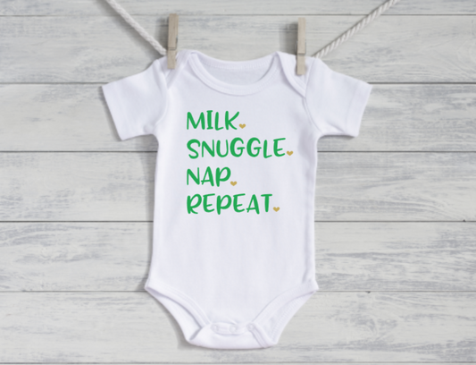 White baby onesie with green text on a wooden background