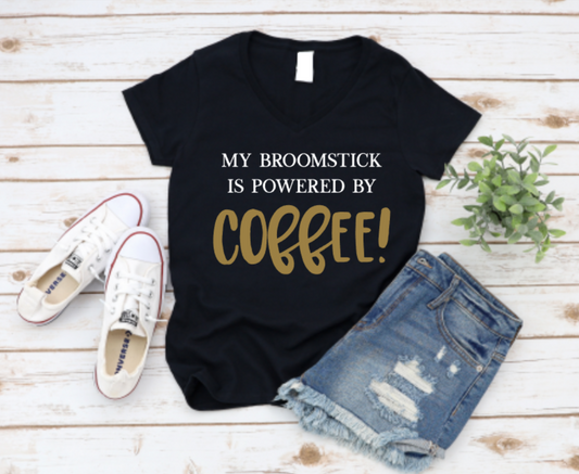 Black t-shirt with 'My broomstick is powered by coffee!' text, paired with white sneakers and denim shorts on a wooden surface. www.missmafia.com