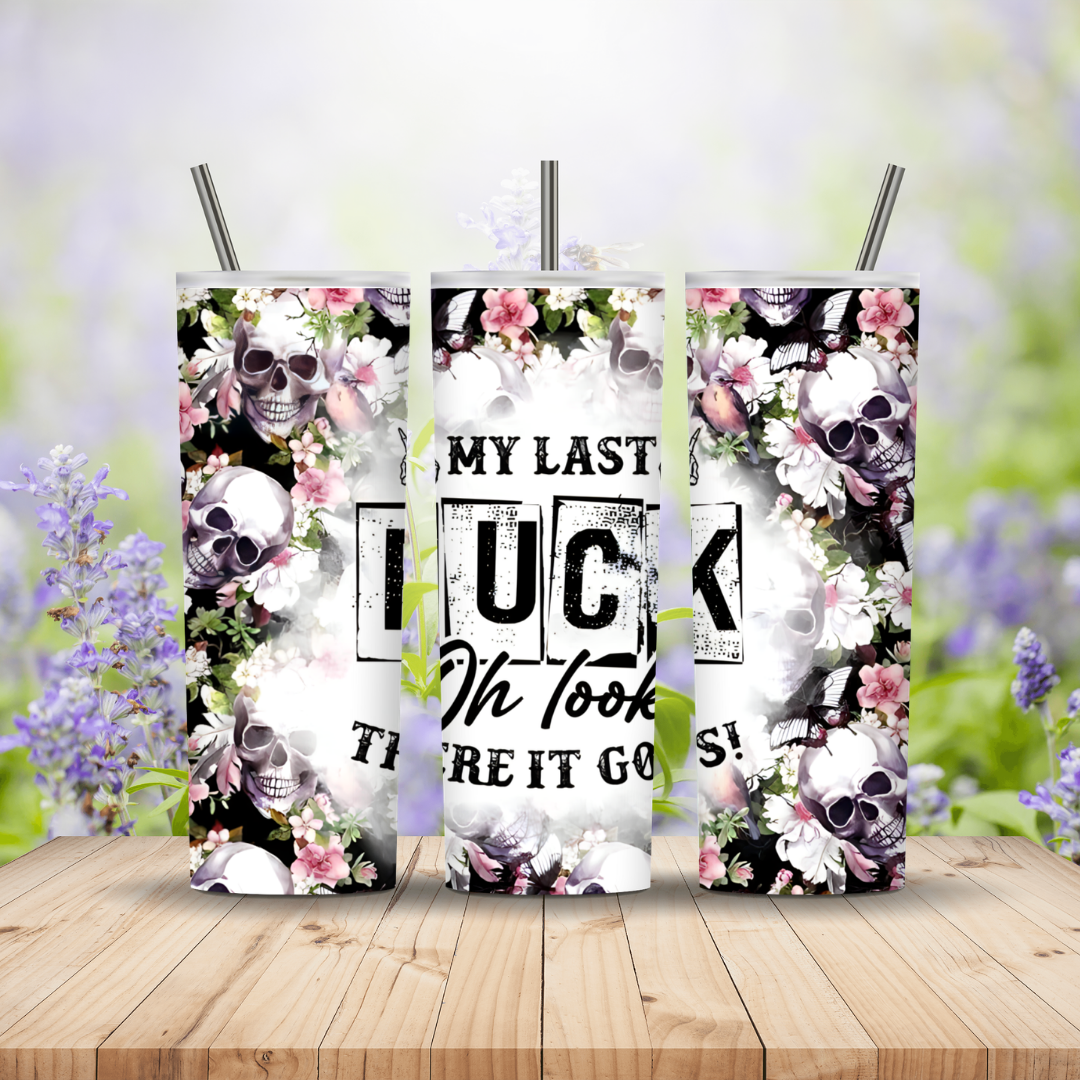 Three decorative tumblers with skull and floral designs on a wooden surface with a blurred floral background.