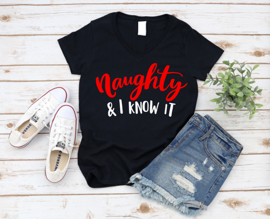 Black t-shirt with 'Naughty & I know it' text, white sneakers, and denim shorts on a wooden surface. www.missmafia.com
