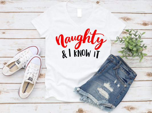White t-shirt with 'Naughty & I Know It' text, denim shorts, and white sneakers on a wooden surface. www.missmafia.com