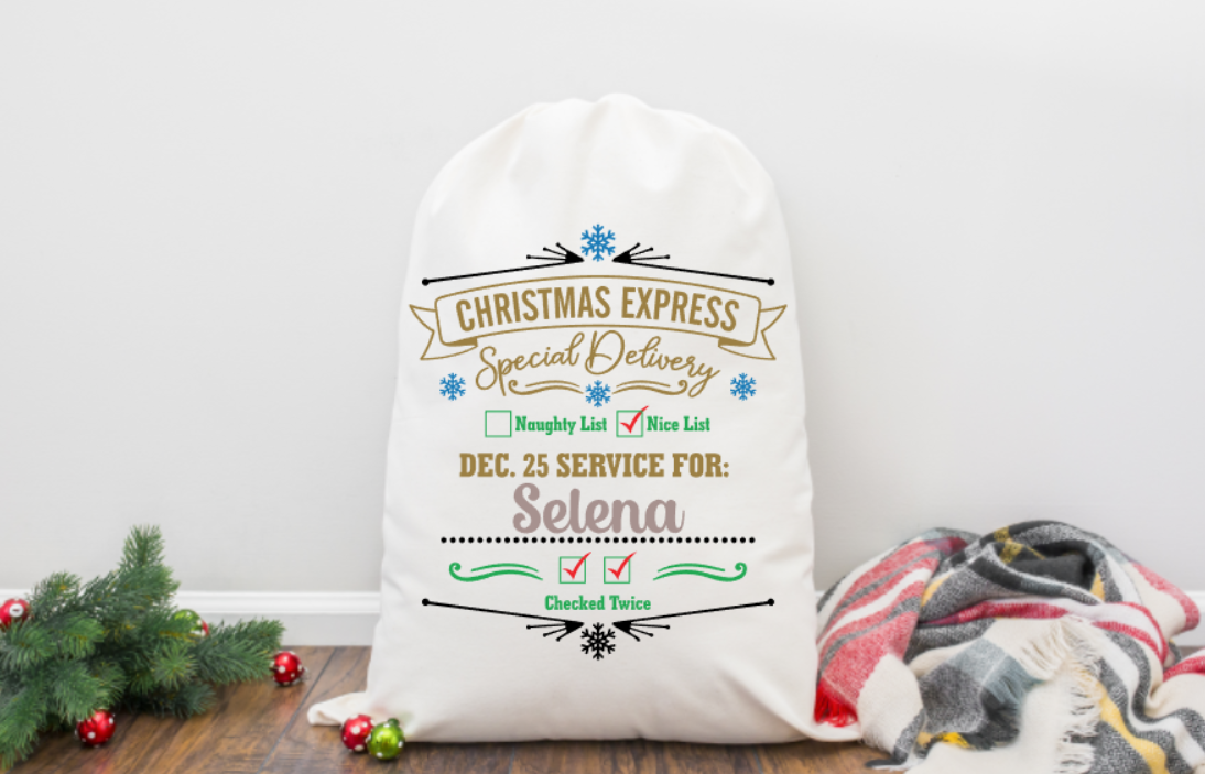 Personalized Christmas sack with decorative text on a wooden floor with a blanket and tree.