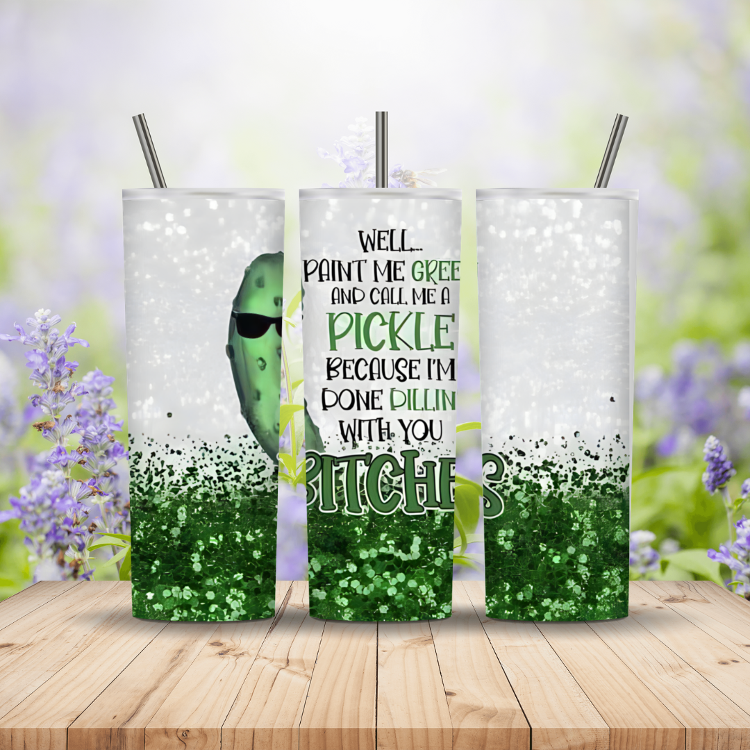 Three tumblers with a pickle design and humorous text on a wooden surface with a blurred floral background.
