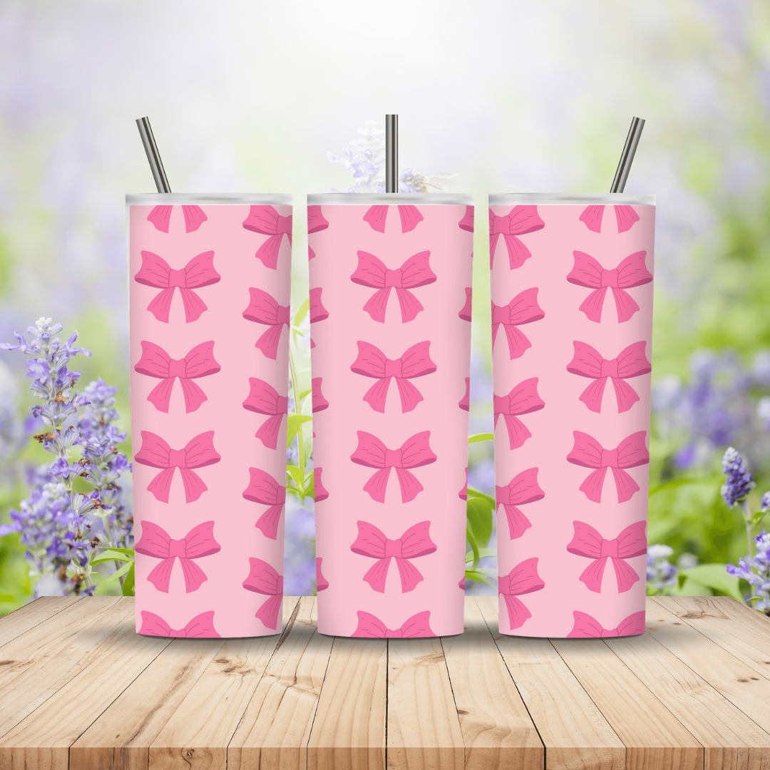 Three pink tumblers with bow pattern on a wooden surface with a blurred floral background