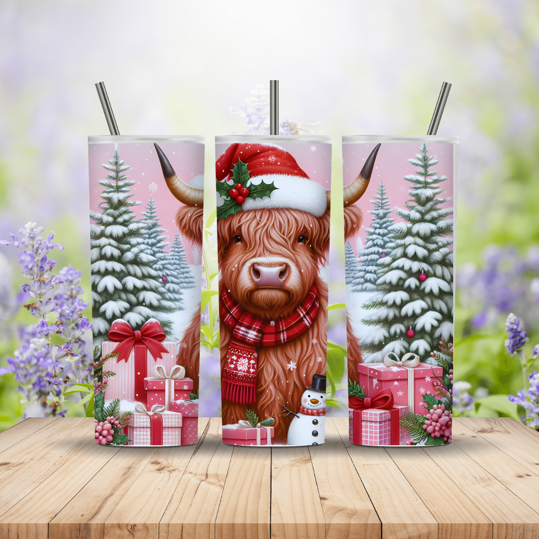 Three Christmas-themed tumblers with a highland cow, Santa hat, and snowy trees on a wooden surface.