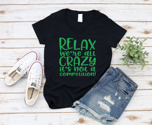 Black t-shirt with green text 'Relax we're all crazy it's not a competition!' on a wooden surface with sneakers and shorts. www.missmafia.com
