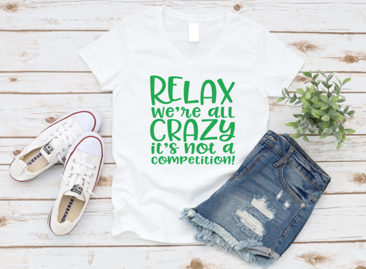 T-shirt with 'Relax, we're all crazy, it's not a competition!' text, paired with denim shorts and white sneakers on a wooden surface. www.missmafia.com