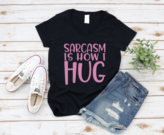 Black t-shirt with 'Sarcasm is how I Hug' text, paired with denim shorts and white sneakers on a wooden surface. www.missmafia.com