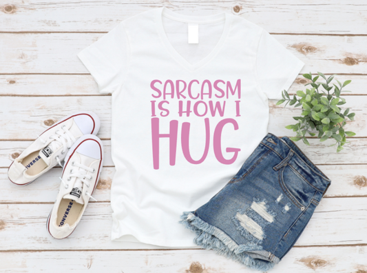 White t-shirt with 'Sarcasm is how I hug' text, denim shorts, and white sneakers on a wooden surface. www.missmafia.com