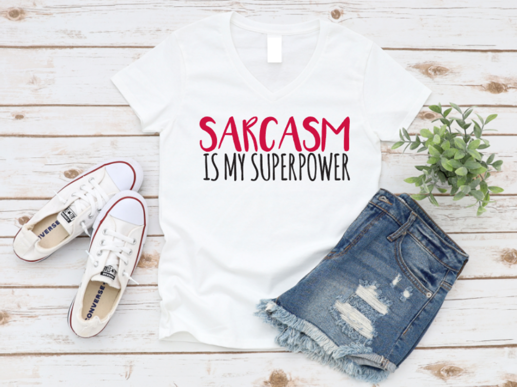 White t-shirt with 'Sarcasm is my superpower' text, paired with denim shorts and white sneakers on a wooden surface. www.missmafia.com