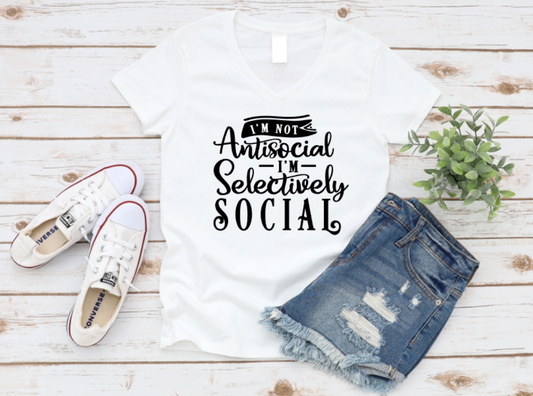 White t-shirt with 'I'm not antisocial, selectively social' text, paired with denim shorts and white sneakers on a wooden surface. www.missmafia.com