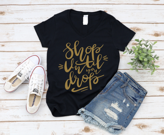 Black t-shirt with gold text, white sneakers, and denim shorts on a wooden surface. www.missmafia.com
