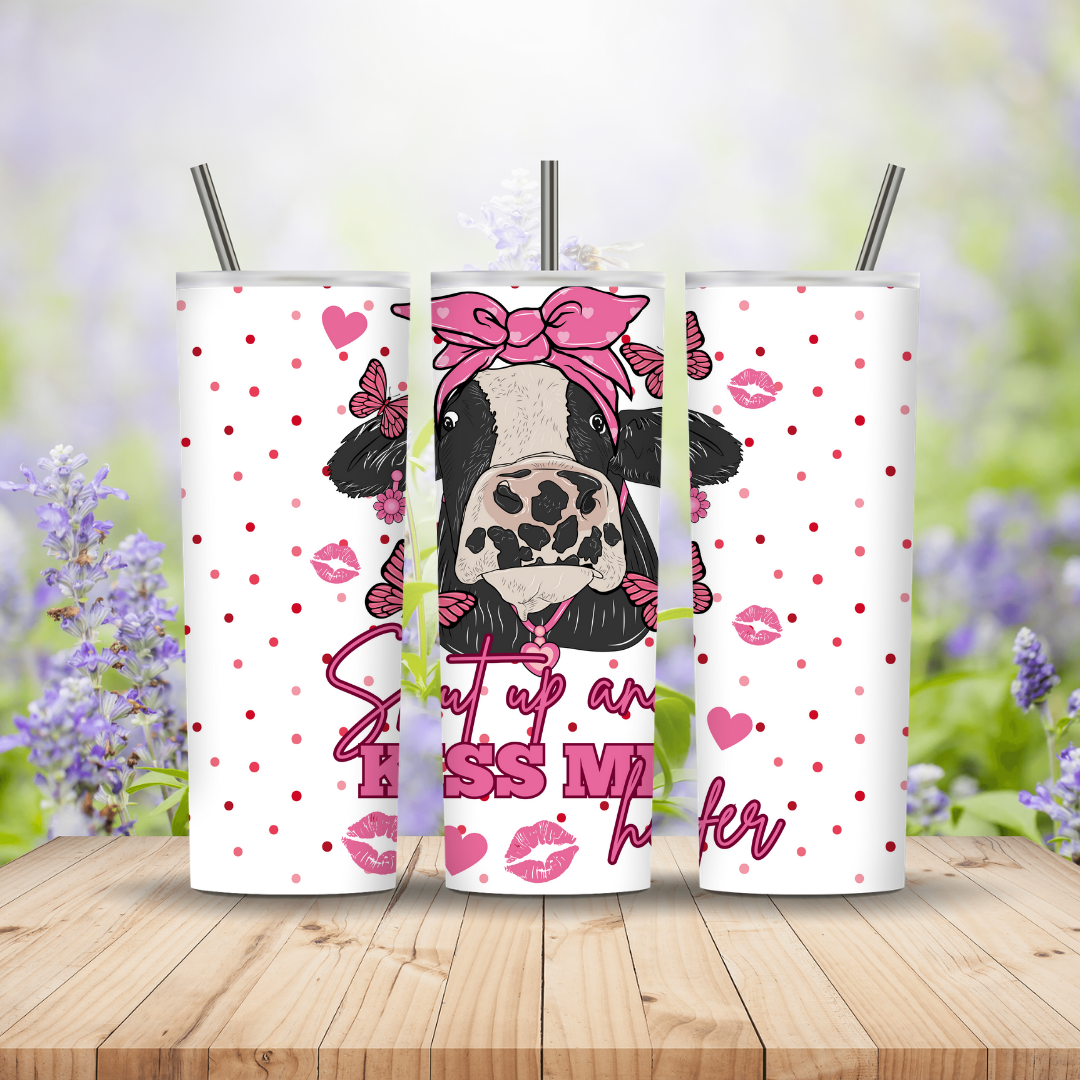Three tumblers with a cow design and text on a wooden surface with a blurred floral background