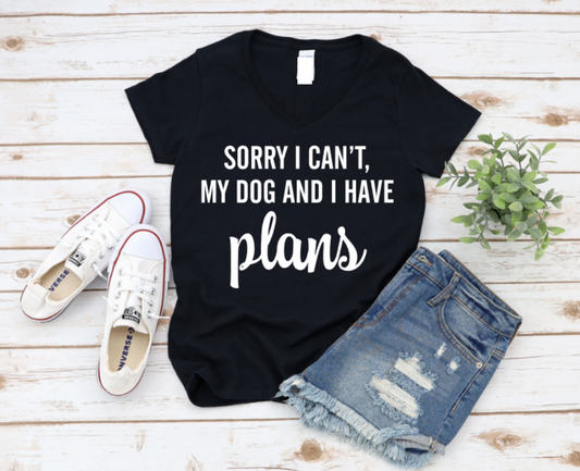 Black t-shirt with 'Sorry I can't, my dog and I have plans' text on a wooden surface with shoes and shorts. www.missmafia.com