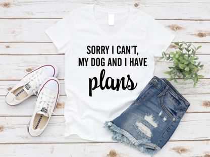 White t-shirt with 'Sorry I Can't, My Dog And I Have Plans' text, paired with denim shorts and white sneakers on a wooden surface. www.missmafia.com