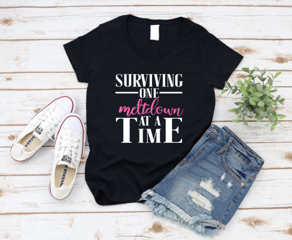 Black t-shirt with 'Surviving one meltdown at a time' text, paired with denim shorts and white sneakers on a wooden surface. www.missmafia.com