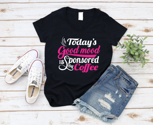 Black t-shirt with 'Today's Good Mood is Sponsored by Coffee' text, paired with white sneakers and denim shorts on a wooden surface.