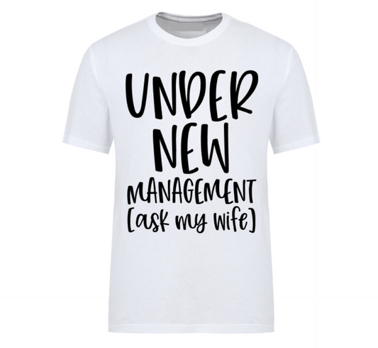 White t-shirt with bold black text reading “Under New Management – See Wife for Details,” styled with casual denim and sneakers—funny gift for husbands or newlyweds.
