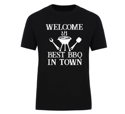 Black t-shirt with bold black text reading “Welcome Best BBQ in Town,” featuring grilling utensils and a barbecue grill graphic – perfect for BBQ dads, weekend warriors, and summer cookout kings.