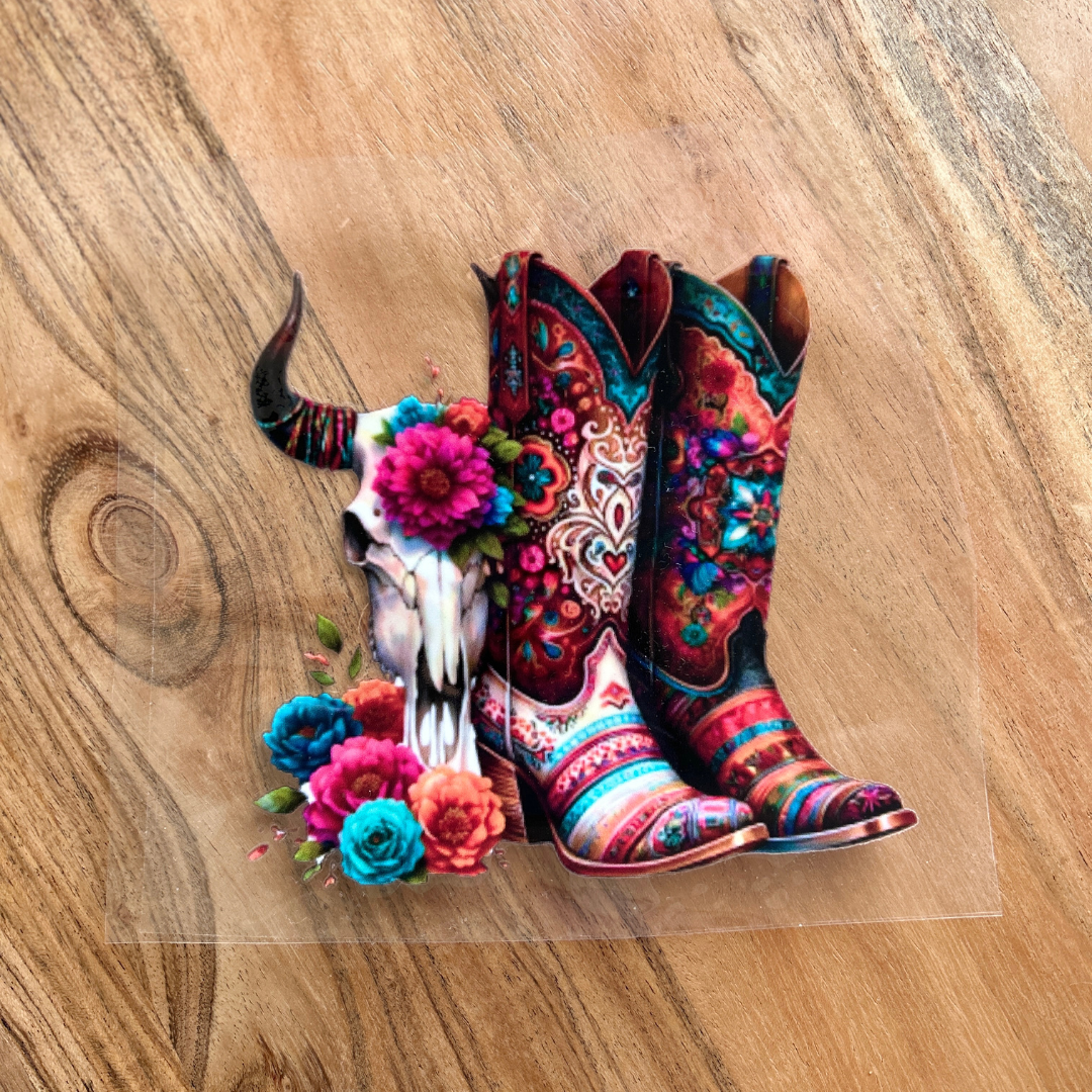Colourful Western-themed UV DTF sticker featuring floral cowboy boots and a bull skull with bright flowers – Miss Mafia custom decal on wood background