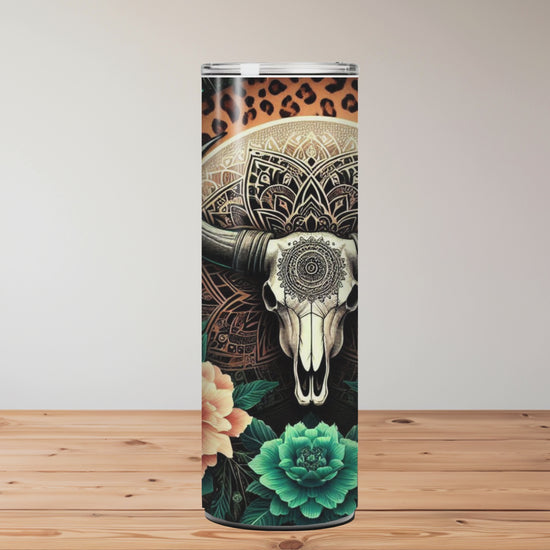 20oz stainless steel tumbler with a boho-western design featuring a mandala bull skull, surrounded by teal succulents, orange florals, feathers, and a starry leopard-print background. Miss Mafia