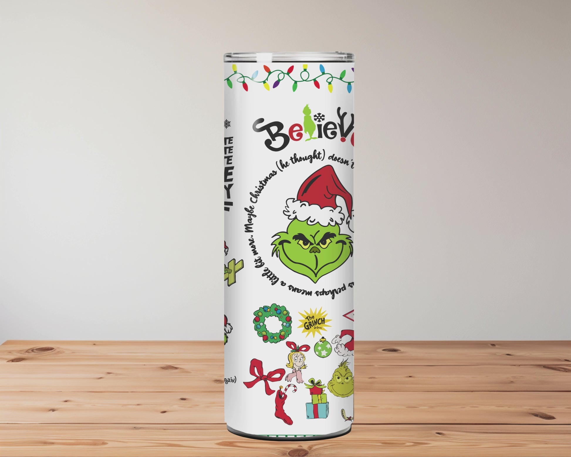 Christmas-themed tumblers with designs and text on a wooden surface with blurred floral background
