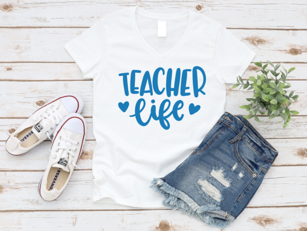 White t-shirt with 'Teacher Life' text, denim shorts, and white sneakers on a wooden surface. www.missmafia.com